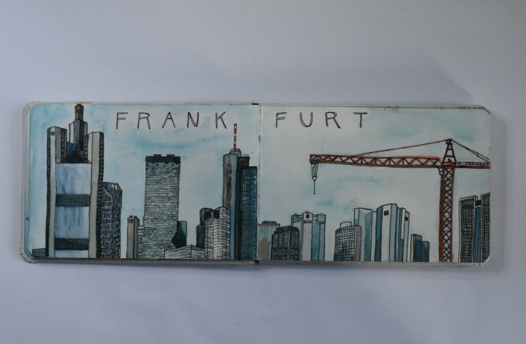 Skizzenbuchseite mit der Frankfurter Skyline und einem Baukran, in Aquarell und Tusche, mit dem Schriftzug ‚Frankfurt‘